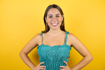 Young beautiful woman over isolated yellow background smiling with arms in waist