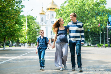 Happy family walking together. Pregnant mother, father and son spend time on city street.