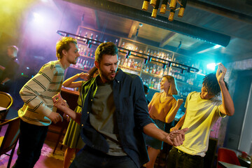 Handsome caucasian young man enjoying evening, celebrating, dancing at party in the bar. People having fun in the background