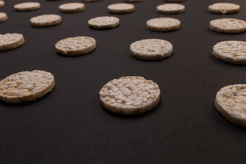 Fototapeta na wymiar Pattern distribution of rice crackers. Round rice crackers, spread out on a black background. Front or perspective design. Low key photography.