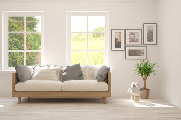 Obraz premium White living room with sofa and summer landscape in window. Scandinavian interior design. 3D illustration