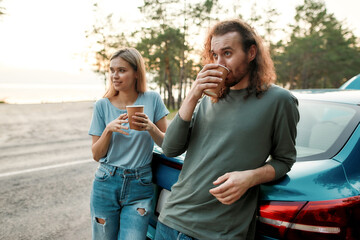 Young couple, man and woman drinking hot coffee or tea after repairing the car during their road trip