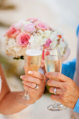 closeup of wedding couple holding champagne glasses with bridal bouquet in background