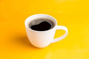 Taza de café blanca sobre fondo amarillo.  Café americano negro