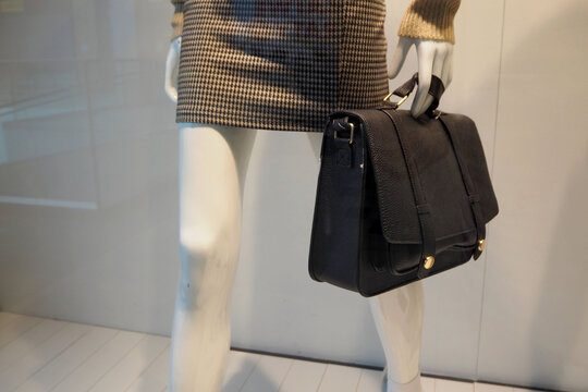 a black leather female briefcase holds a plastic mannequin in a gray skirt in a boutique window