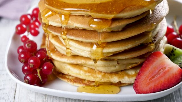 stack of pancake with syrup pouring and fresh fruits