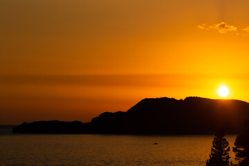 Orange sunset with silhouettes in the sea with mountains, beautiful perfect landscape in the evening by the sea