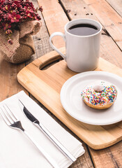 Fotografía de mini dona de vainilla con chispas de colores y una taza de café sobre fondo rustico.