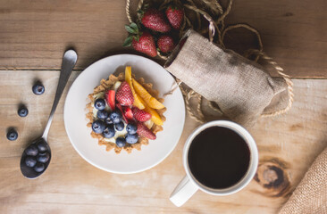 fotografía cenital de un postre tartaleta de frutas y una taza de café sobre una mesa de madera.