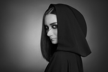 Mysterious witch in mantle with hood on dark background. Black and white effect