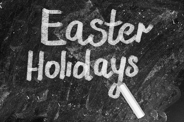 Text Easter Holidays and chalk on blackboard, top view. School break