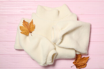 Warm sweater and dry leaves on pink wooden background, flat lay. Autumn season