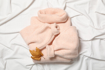 Fototapeta na wymiar Pink warm sweater and dry leaf on white fabric, top view. Autumn season