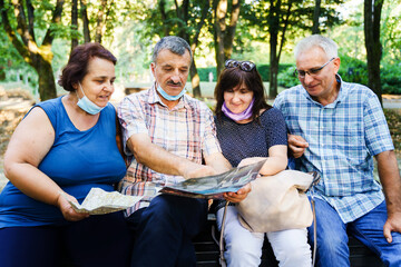 Group of senior friends tourists in autumn or summer day - Mature man showing to his wife and company location on the map and instructions about the route - real people tourism concept