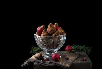 Chocolate truffles covered in cacao powder and red baubles against the black background. Christmas dessert
