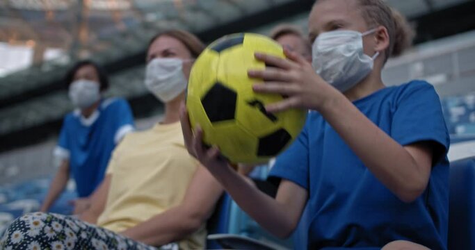 Family on fooball match during coronavirus covid 19 pandemic, group of friends wearing medical protection masks watching soccer game and emotionally rooting for favorite team. Safe holidays post covid