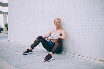 Good looking bodybuilder with perfect slim figure resting at city urbanity, Caucasian female athlete with muscular body holding water tumbler thinking about crossfit exercises for energy workout