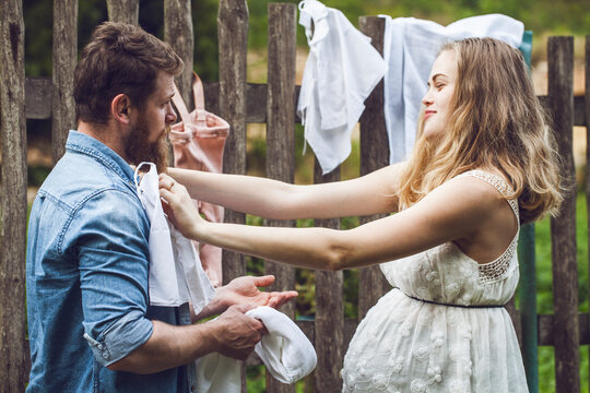 Man with pregnant woman hanging out the laundry at the fence