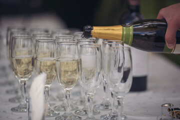 Party and holiday celebration concept. Many glasses of champagne on the table in the restaurant. The process of bottling champagne in glasses. The waitress pouring champagne in a glass.