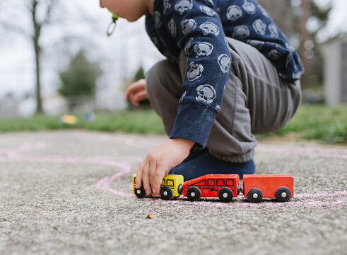 boy plays with trains on sidewalk