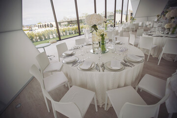 Wedding. Banquet. The chairs and round table for guests, served with cutlery, flowers and crockery and covered with a tablecloth.Elegant tablescape. White dinner table decorated with white flowers.
