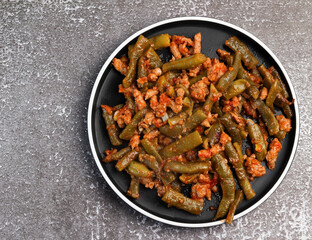 Green beans with tomato sauce and minced meat on a round plate on a dark background. Top view, flat lay