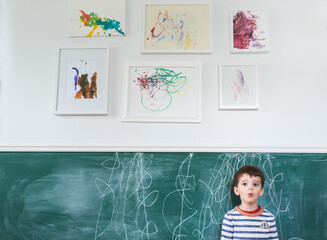 boy stands in front of scribbles on chalkboard