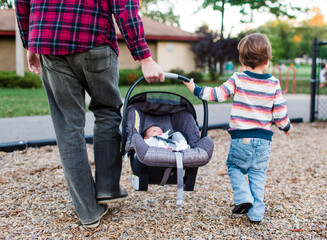 boy helps dad carry baby sister in car seat