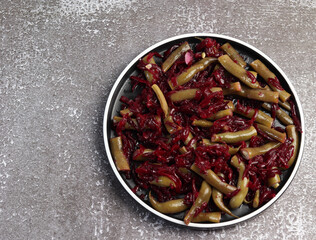 Beet and green bean salad on a round plate on a dark background. Top view, flat lay