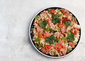 Rice with hot pepper and ham on a round plate on a light gray background. Top view, flat lay
