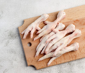 Raw chicken feet on a rectangular wooden cutting board on a light gray background. Top view, flat lay
