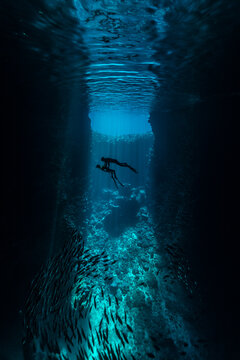 A couple of freedivers handing diving in the cave with sun rays