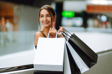 Fashion woman in black dress with shopping bags enjoying shopping in the mall. Black friday, sale, consumerism, lifestyle concept.