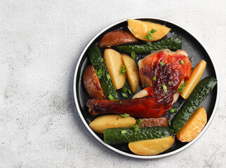Backed chicken with potatoes on a round plate on a light gray background. Top view, flat lay