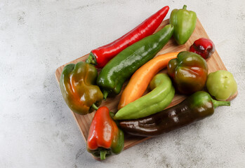 Assorted bell peppers on a rectangular cutting wooden board on a light gray background. Top view, flat lay