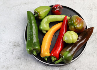 Assorted bell peppers on a round plate on a light gray background. Top view, flat lay
