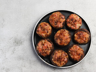 Champignons stuffed with ham and cheese on a round plate on a light gray background. Top view, flat lay