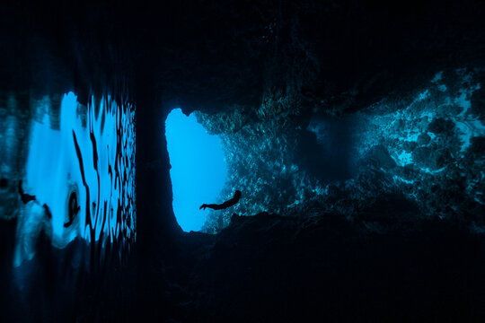 A female freediver diving into the cave with backlit