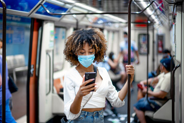 African American woman with mask using smartphone inside the train.