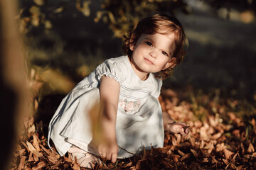 Little brunette girl plays with leaves in the park. Autumn time