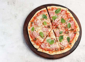 Pizza with ham and olives on a round wooden cutting board on a light gray background. Top view, flat lay