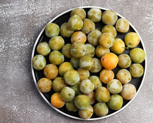 Ripe green plums on a round plate on a dark background. Top view, flat lay