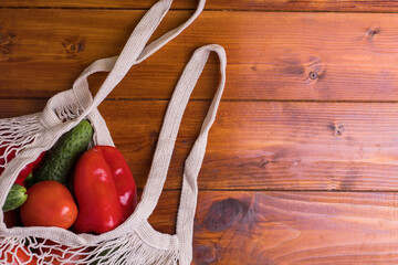 Eco bag string bag with vegetables cucumbers and tomatoes on a wooden background. Zero West