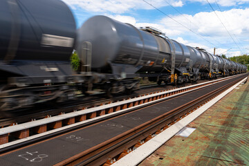 Fototapeta na wymiar Blurry photo of railroad tank cars in motion, on a metal bridge over the river.