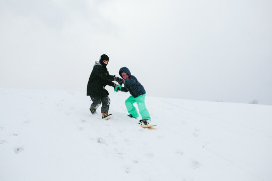 child helps another snowboard down hill