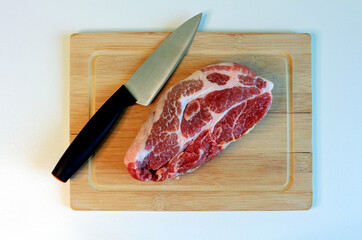 Fresh piece of raw meat with a sharp knife on a wooden cutting board. Top view.