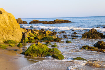 a gorgeous set of rocks at the beach covered in lush green algae with ocean waves rolling in at El Matador beach in Malibu California