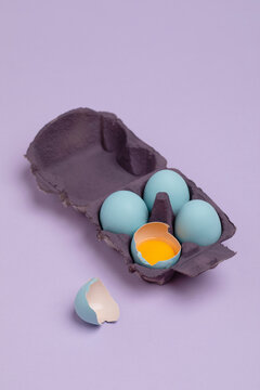 three colored eggs in cardboard with one broken egg