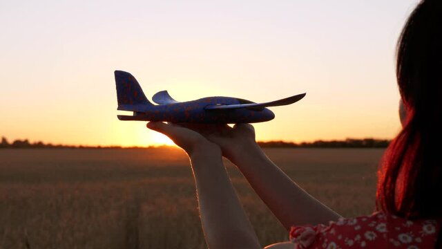 A girl holds a toy airplane in her hands against the background of the sunset. The concept of air tourism, travel.