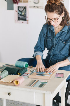 Focused Young Woman Choosing Color Sample For Moodboard On Wooden Table